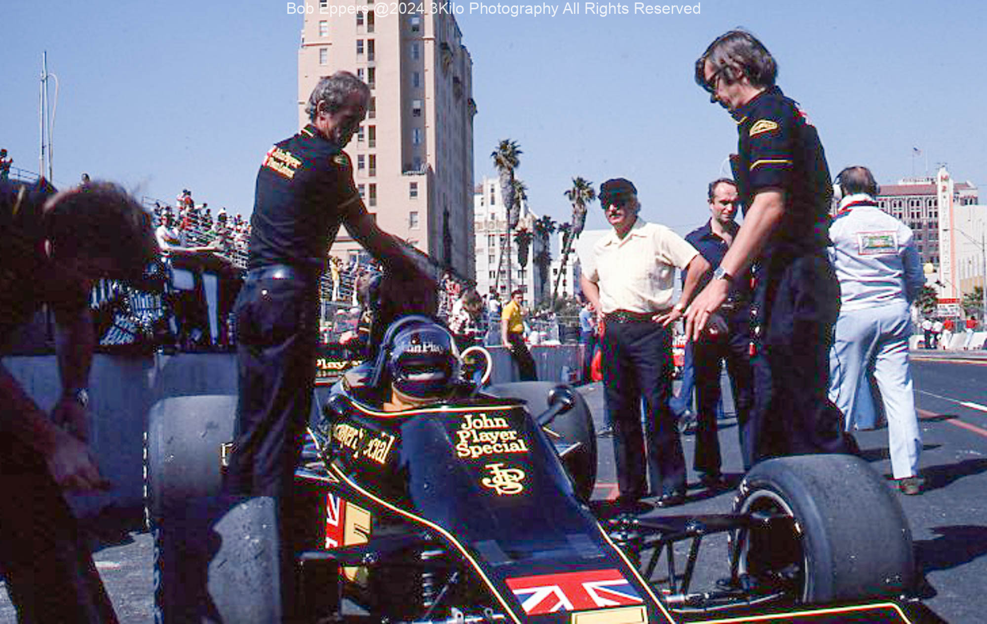 Photo of F1 Lotus in the pit lane,  Colin Chapman is at the rear wearing a hat.  1976
